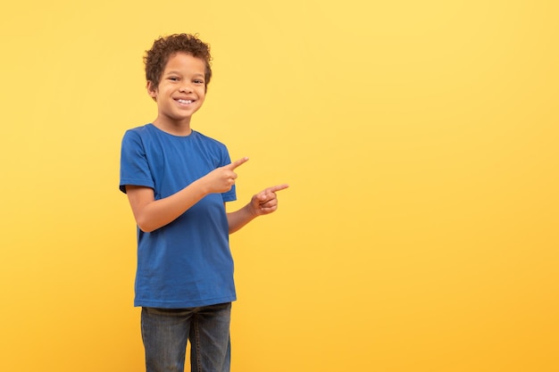 Photo boy pointing sideways at free space on yellow background