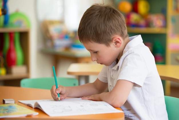 テーブルの少年未就学児は書くことを学ぶ