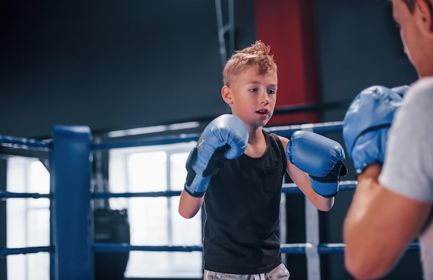 Boy in protective gloves have sparring with trainer on the\
boxing ring.