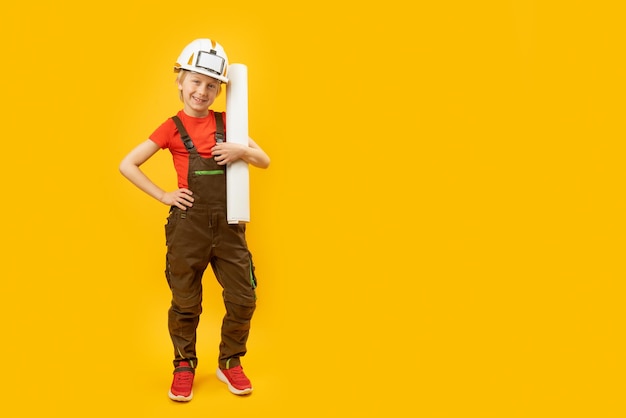 Boy in protective helmet overalls and with sheet of paper in his hands child as builder or architect copy space mockup