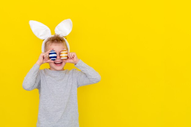 Ragazzo in orecchie da coniglio coniglietto sulla testa con uova colorate su giallo