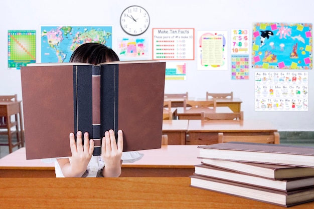 Photo boy reading book at desk in classroom