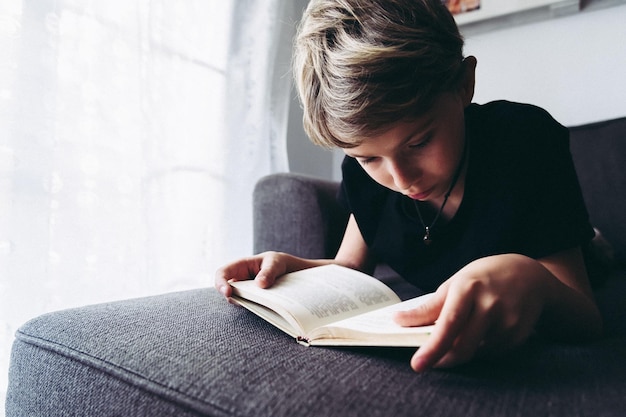 Boy reading book on sofa at home