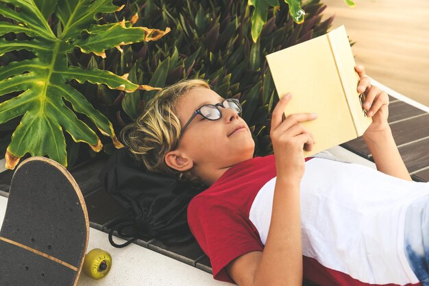 Photo boy reading book while lying on retaining wall