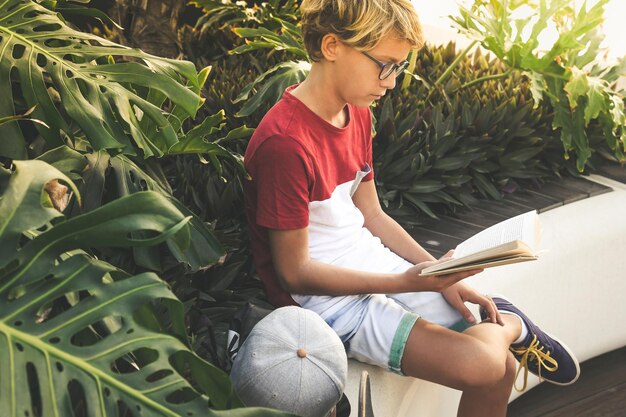 Boy reading book while sitting by plants