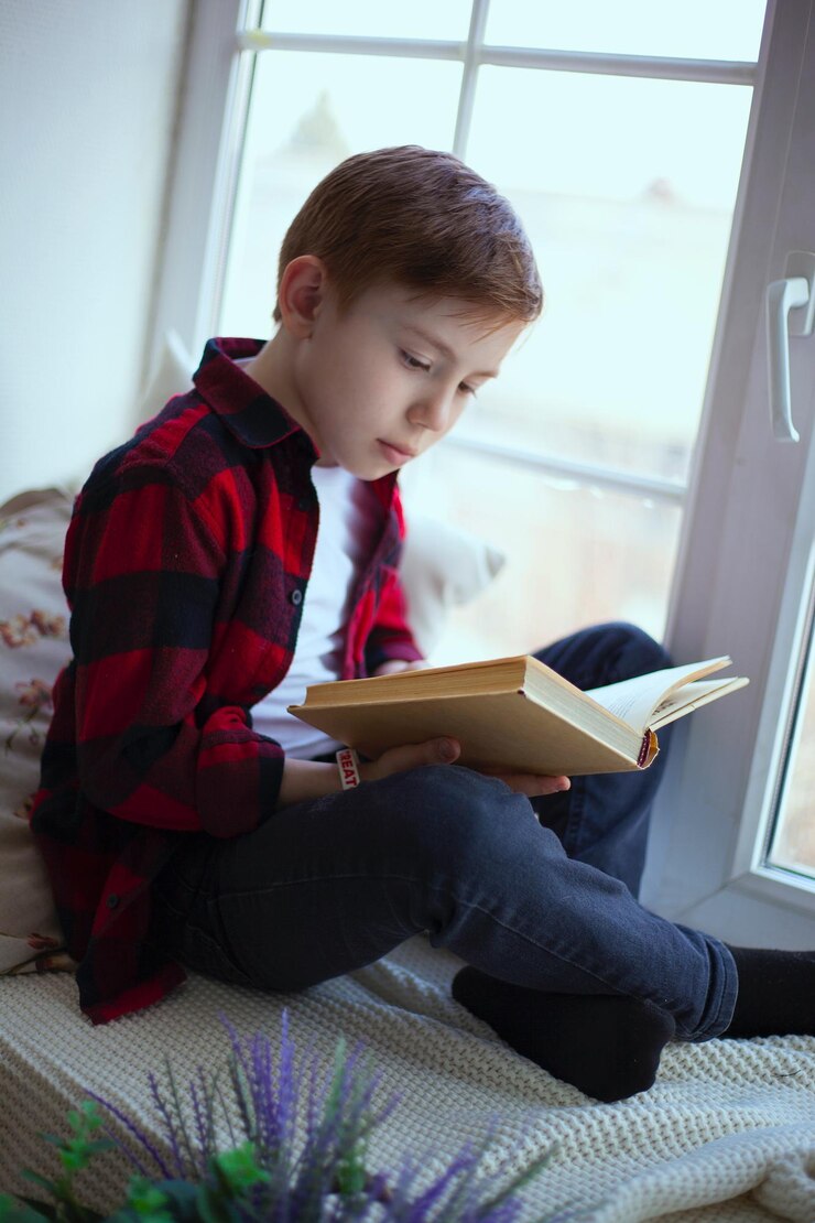 फोटो boy reading book while sitting by window at home