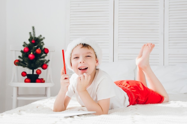 Il ragazzo con un berretto rosso scrive una lettera a babbo natale