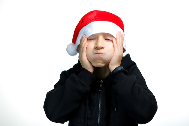 A boy in a red Santa hat puffed out his cheeks and looks at the camera