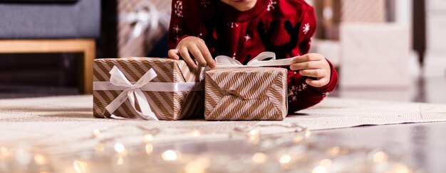 A boy in a red sweater lies on the carpet and hugs gifts