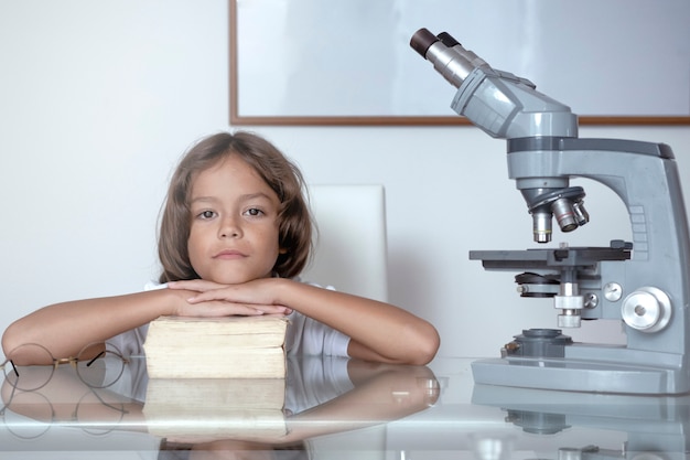 Boy resting on book, next to a microscope