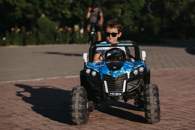 boy rides in a toy mini car in the park in summer