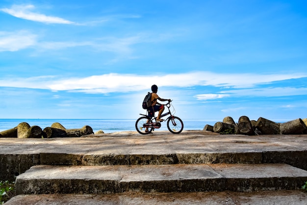 写真 空の向こうの岩の上で自転車に乗っている少年