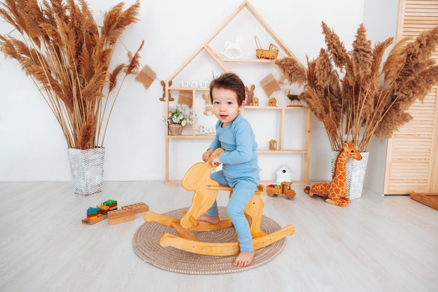 A boy riding a wooden rocking horse toy in a white bedroom with decor A child is playing in the nursery Toys for kids children's interior