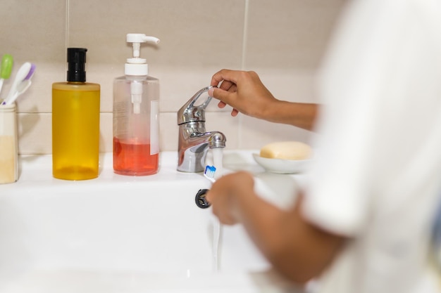 Ragazzo che risciacqua lo spazzolino da denti sotto l'acqua corrente del rubinetto nel lavandino del bagno