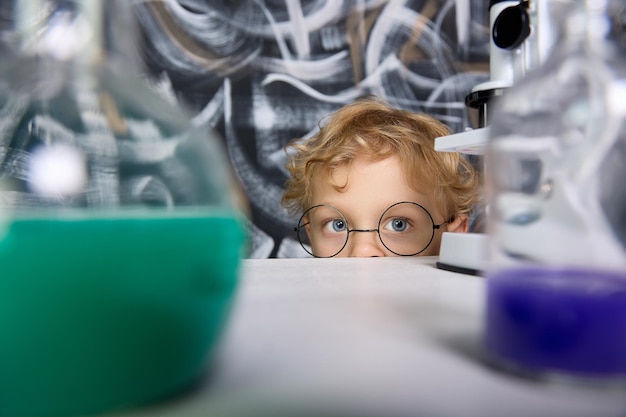 Boy in round glasses watches the reaction of substances in test tubes