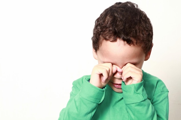 Boy rubbing eyes against white background