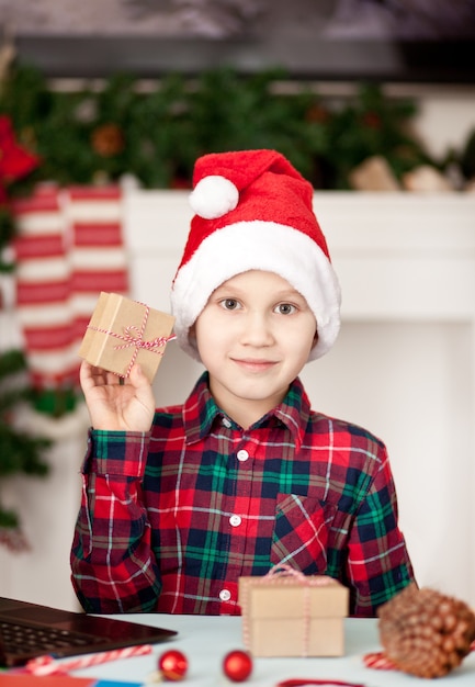 мальчик в шапке Санта-Клауса держит подарочную коробку