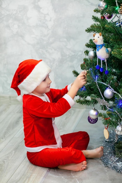 A boy in a Santa costume is decorating a Christmas tree