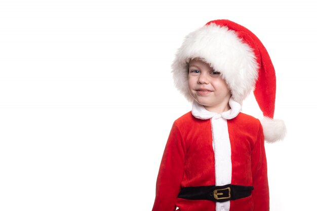 A boy in a Santa suit on a white background looks into the frame .