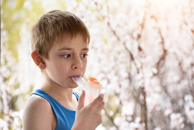 Boy of school age in breathing mask inhaler on a background of flowering trees. Home treatment. Prevention