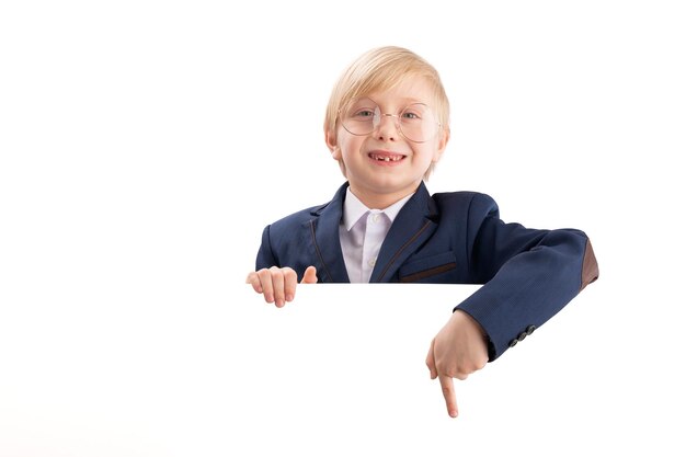 Boy in school uniform and large glasses with blank white poster board peeking Schoolboy points his finger at something Copy space