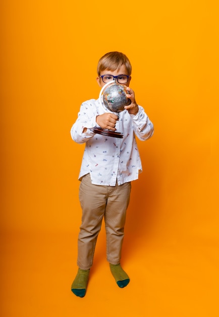 Boy schoolboy 7 years old schoolboy in glasses with a globe in his hands smiling on a yellow background