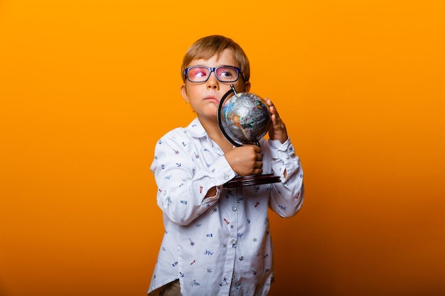 Boy schoolboy 7 years old schoolboy in glasses with a globe in his hands smiling on a yellow background