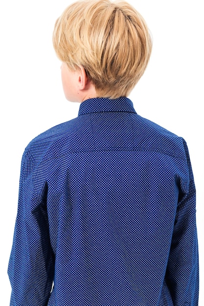 Boy schoolboy posing in a school uniform blue shirt and trousers on a white background The boy stands with his back to the camera showing his shirt from behind Vertical photo