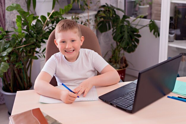 Мальчик школьник за столом и делает домашнее задание на ноутбуке