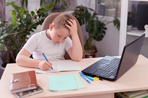 Scolaro del ragazzo al tavolo e fa i compiti su un computer portatile