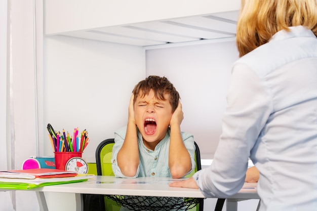 Photo boy screaming while sitting at classroom