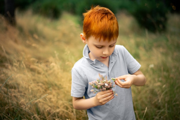 A boy of seven with red hair with a bouquet of wildflowers in summer