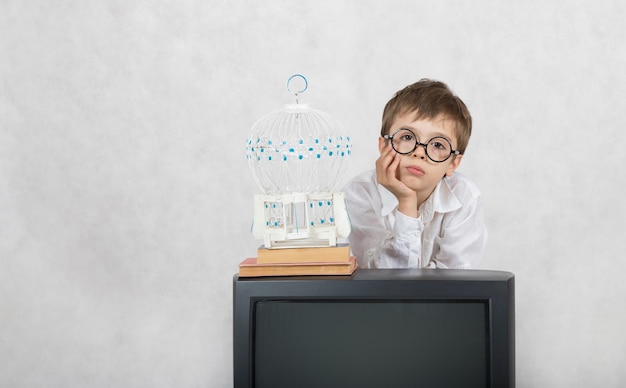 Boy of seven years old looks at white cage which is laced on old TV. Free space for a text.