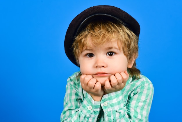 Мальчик в рубашке держит лицо руками. Модный маленький ребенок в кепке. Ретро стиль. Красивый ребенок в шляпе.
