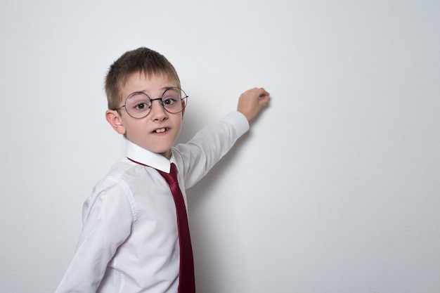 Boy in shirt, tie and glasses writes on the board. High school student. Copy space