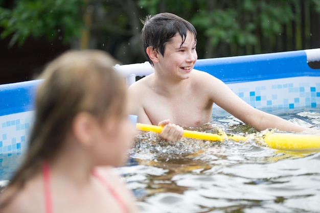 A boy shoots a water pistol in the pool at summer day