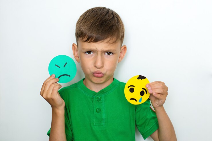 The boy shows emotions and holds sad emoticons made of paper