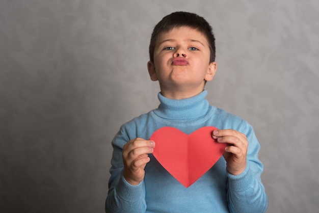 The boy shows heart of red paper The child holds a valentine in the form of a heart