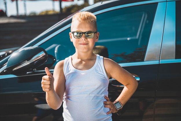 Boy shows thumb on the background of the car