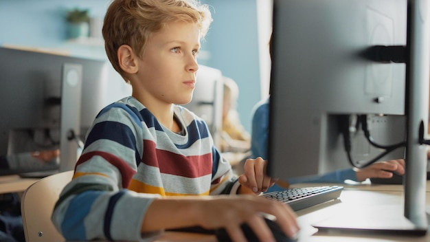 A boy sits at a desk and works on a computer.