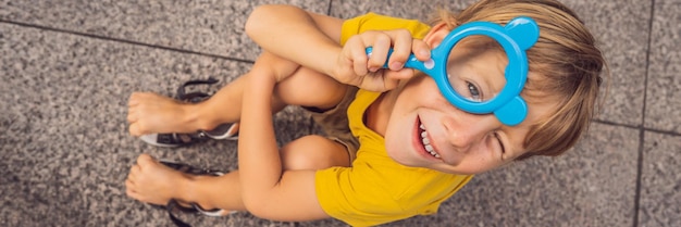 Boy sits on the floor and looks into a magnifying glass banner long format