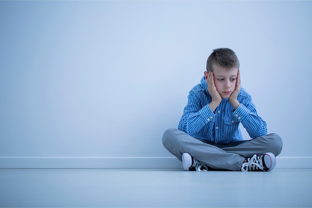 A boy sits on the floor with his hands on his head.