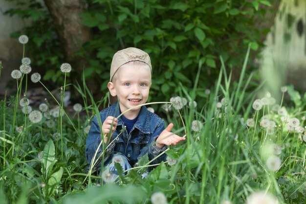 The boy sits on the grass and holds a dandelion in his handx9xA