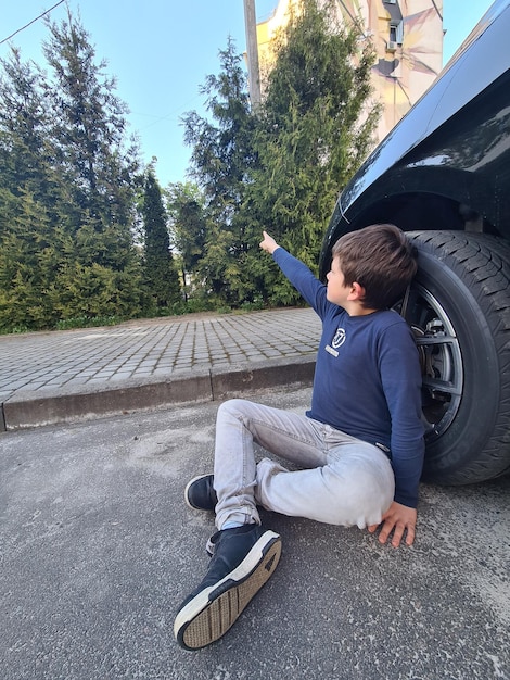 Photo a boy sits on the ground in front of a car with a blue shirt that says's on it.