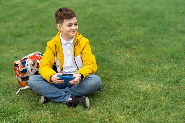 Мальчик сидит на лужайке со смартфоном
