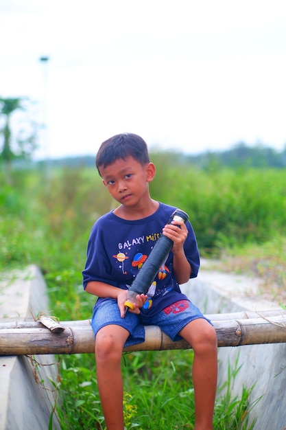 A boy sits on a log with a fishing rod in his hand.