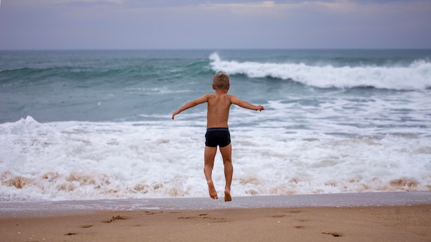 Boy sits on the ocean shore with his arms open towards wind and waves Storm in summer courage