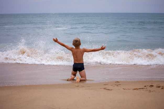 Boy sits on the ocean shore with his arms open towards wind and waves Storm in summer courage