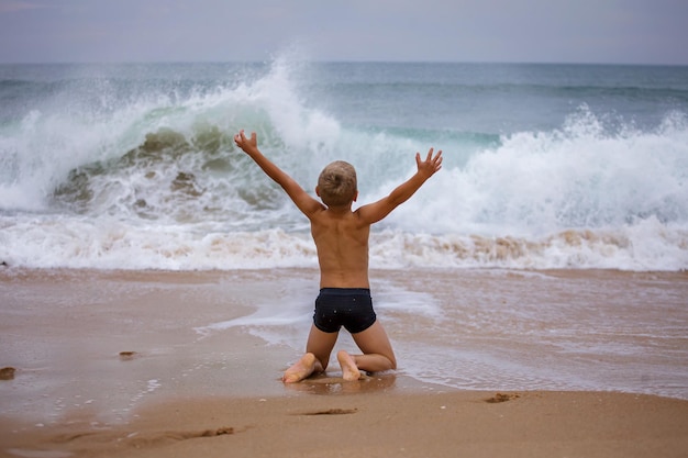 写真 少年は風と波に向かって腕を広げて海岸に座っている夏の勇気の嵐