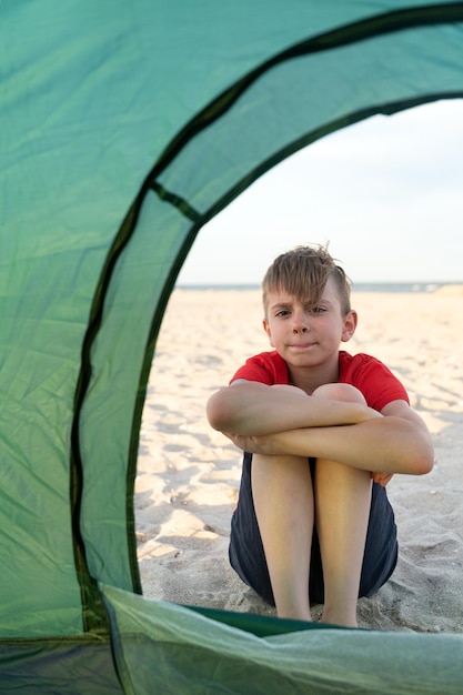 Boy sits outside tourist tent Vertical frame Camping holiday in countryside